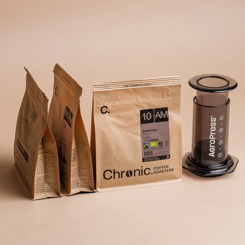 3 paquets de cafés Chronic. et une Aeropress sur fond beige